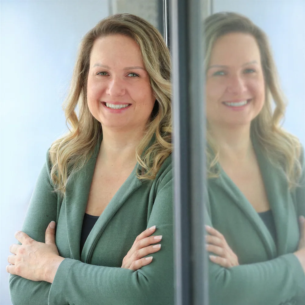 Stefanie Zingler lehnt lächelnd an einer Glaswand, die Arme verschränkt.